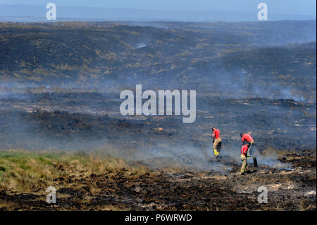 Bolton, Lancashire, UK. 2 juillet, 2018. Les pompiers de Lancashire et autres forces continuent de s'attaquer à un énorme incendie landes sur la colline d'hiver près de Bolton, Lancashire. Le brasier a été commencé et délibérément fait rage pendant six jours couvrant une superficie de 7 kilomètres carrés. Les pompiers dans le paysage carbonisé battre la masse couvant pour aider à arrêter la propagation du feu. Banque D'Images