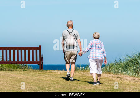 West Bay Beach, North Berwick, East Lothian, Écosse, Royaume-Uni, 3 juillet 2018. La canicule en Écosse se poursuit. Un couple plus âgé tient la main tout en marchant le long de la côte sur Elcho Green, par une journée ensoleillée avec le ciel bleu Banque D'Images