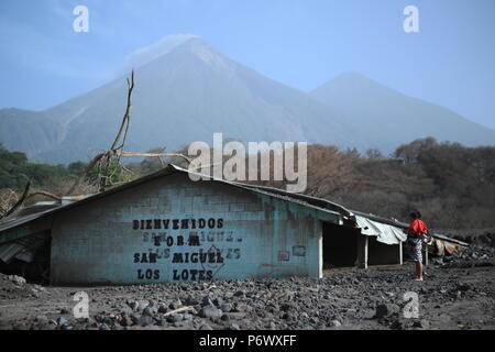 Escuintla, Guatemala. 29 Juin, 2018. "Bienvenue à San Miguel de los LOTES' sur le mur d'une maison qui a été touchée par l'éruption volcanique il y a un mois. Le refuge a été mis en place pour les personnes qui ont été effectués par l'éruption volcanique sur le 3 juin. L'homme est maintenant en attente d'être portée à nouveau logement d'urgence. L'éruption a tué au moins 110 personnes. Les données du gouvernement indiquent que 186 maisons ont été complètement détruites et 750 autres ont été gravement endommagées. Credit : Morena Perez Joachin/dpa/Alamy Live News Banque D'Images