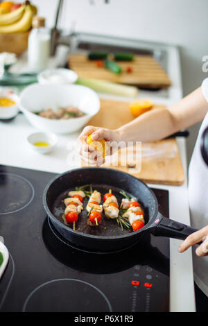 Portrait de jeune femme au foyer heureuse pour le dîner de la viande de poulet à frire sur plaque de cuisson vitrocéramique. Banque D'Images