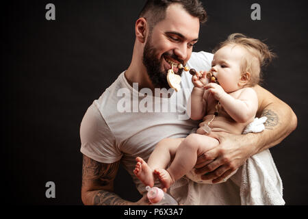 Studio shot of playful Père vêtu de blanc T-shirt bébé fille bébé et jouer avec chapelet isolé sur fond noir Banque D'Images