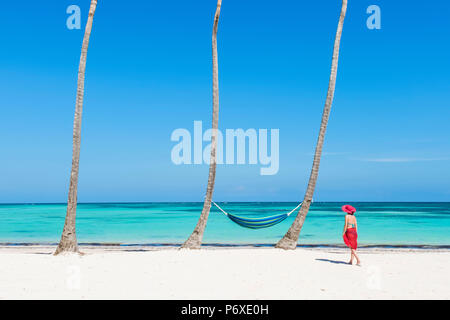 Juanillo Beach (playa Juanillo), Punta Cana, République dominicaine. Femme marche sur une plage bordée de palmiers (MR). Banque D'Images