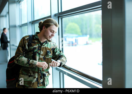 L'homme de race blanche à l'aéroport à regarder à la salle d'attente, le port de la veste de camouflage et sac à dos. Banque D'Images