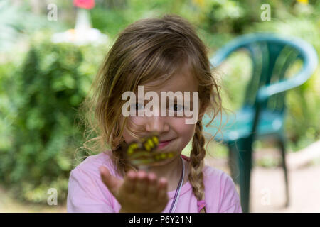 Sourire petite fille blonde avec un papillon jaune repéré dans sa main. Focus sélectif. Plan rapproché. Banque D'Images