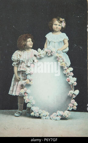 Vintage peint à la photographie d'vers 1908 avec deux jeunes filles avec un emblème de fleurs Banque D'Images