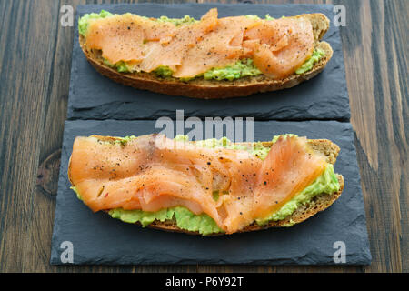 Le seigle des toasts avec du saumon fumé et guacamole servi sur ardoise plaques. Fond de bois sombre, haute résolution Banque D'Images