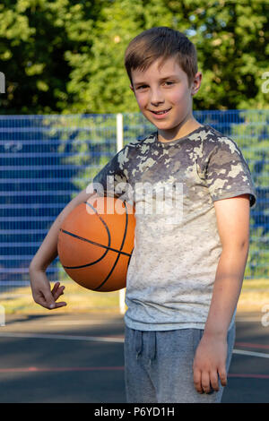 Pre-teen boy holding a basket-ball sur une cour dans un parc Banque D'Images