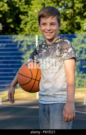 Pre-teen boy holding a basket-ball sur une cour dans un parc Banque D'Images