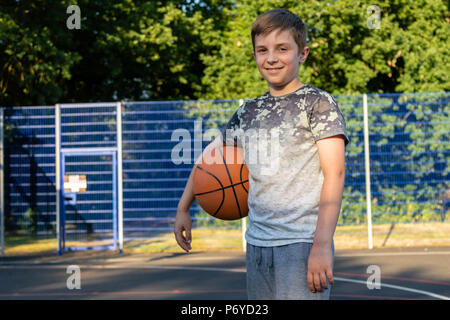 Pre-teen boy holding a basket-ball sur une cour dans un parc Banque D'Images