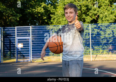 Pre-teen boy holding a basket-ball sur une cour dans un parc Banque D'Images