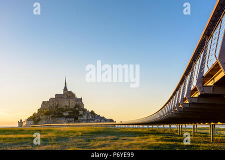 Vue sur le Mont Saint-Michel, l'île de marée au coucher du soleil et la marée basse avec le pont sur pilotis et au premier plan. Banque D'Images