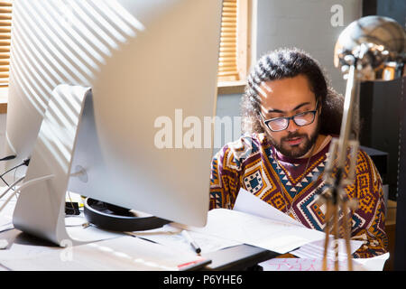 L'accent creative businessman reading paperwork at computer in office Banque D'Images