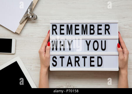 Espace de travail avec tablette, smartphone, feuille et 'N'oubliez pas pourquoi vous avez commencé" mots sur lightbox sur table en bois blanc. Les mains tiennent conseil moderne avec Banque D'Images