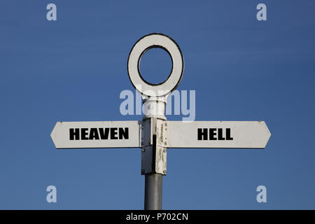 Ancien panneau routier avec le ciel et l'enfer pointant dans des directions opposées contre un ciel bleu Banque D'Images