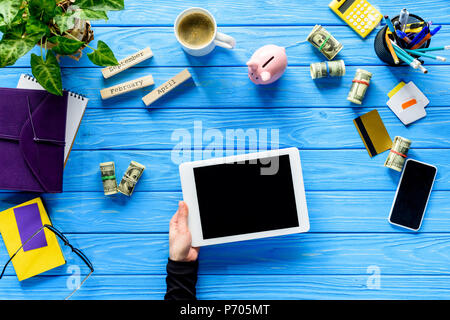 Close-up of hand holding digital tablet sur table en bois bleu avec de l'argent et de papeterie Banque D'Images