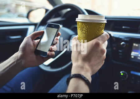 Les bras de l'homme tenir un café et téléphone dans l'automobile Banque D'Images