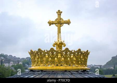 Croix d'or et de la couronne à lourdes france avec ciel sombre. Banque D'Images