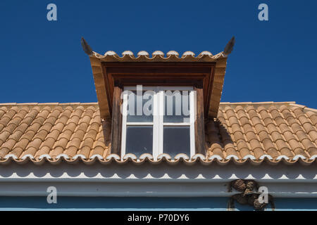Détail d'une maison portugaise. Toit avec de nouvelles tuiles et une fenêtre. Nids d'hirondelle. Ciel bleu clair lumineux. Castro Marim, Algarve, Portugal Banque D'Images