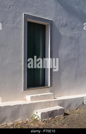 Vue latérale sur une maison à la façade blanche et son entrée de porte verte avec un cadre gris. Deux escaliers. Route avec des pavés. Journée ensoleillée. Cast Banque D'Images