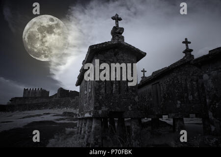 Full Moon Rising au crépuscule sur le château médiéval et les vieux bâtiments de maïs en granit dans un village éloigné de Lindoso, nord du Portugal. Infrarouge analogique utilisé f Banque D'Images