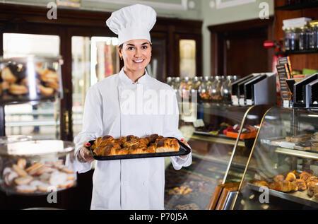 Smiling happy woman baker montrant au chaud délicieux croissants dans une boulangerie Banque D'Images