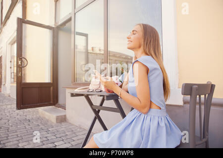 Portrait de femme à la mode la mode moderne message SMS par le smartphone en restaurant en plein air, d'attente, de rencontres. Bouquet de pivoines et de café sur le Banque D'Images