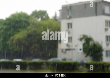 La forte pluie, gouttes vertical contre maisons floues en arrière-plan Banque D'Images