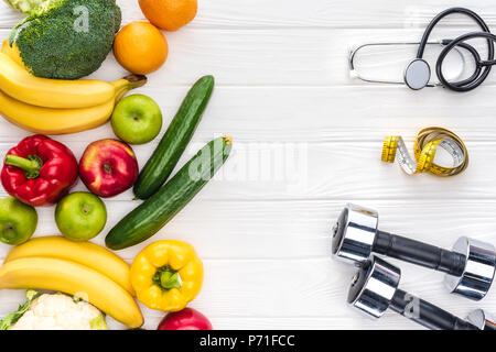Vue de dessus les fruits et légumes frais, des haltères, stéthoscope et ruban à mesurer sur la table en bois Banque D'Images