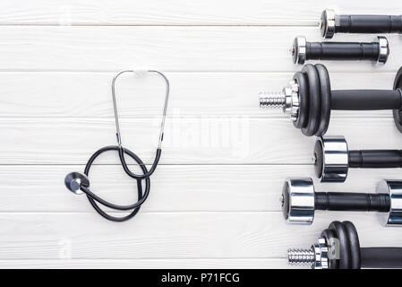 Vue de dessus de divers haltères et stéthoscope sur la surface en bois blanc Banque D'Images