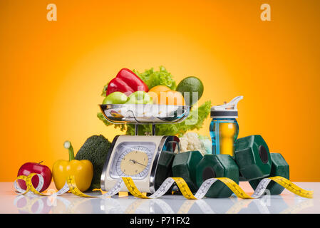 Les fruits et légumes frais sur les balances, bouteille de sport avec de l'eau, des haltères et un ruban à mesurer sur jaune Banque D'Images