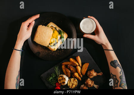 Vue de dessus de personne mangeant végétalien délicieux burger avec frites et boire de la bière sur noir Banque D'Images