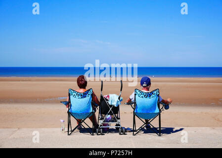 Couple assis dans les mêmes chaises pliantes avec bébé en poussette entre eux sur la plage de Blackpool sur une chaude journée d'été Banque D'Images