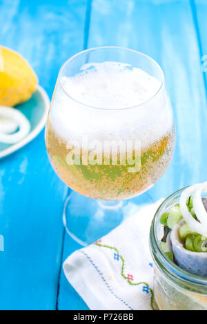 Hareng mariné hollandais traditionnel avec le citron et les oignons dans un bol. La bière belge fraîche dans un verre. Des fruits de mer sur un fond bleu. Copier sapce Banque D'Images