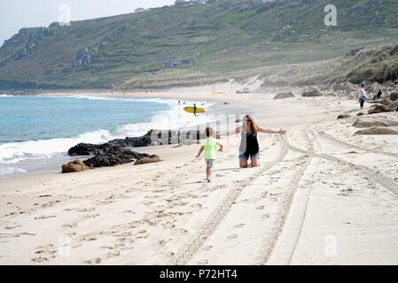 Petit garçon courir vers sa mère qui a les bras grands ouverts prêt à l'étreindre, sur la plage de Sennen Cove sur un été, Cornwall England UK Banque D'Images