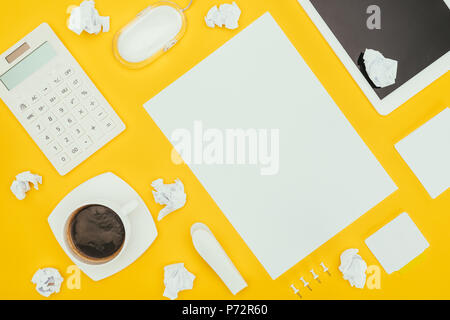 Vue de dessus de feuille de papier vierge, papiers froissés, notes, calculatrice et tablette numérique isolé sur le jaune Banque D'Images