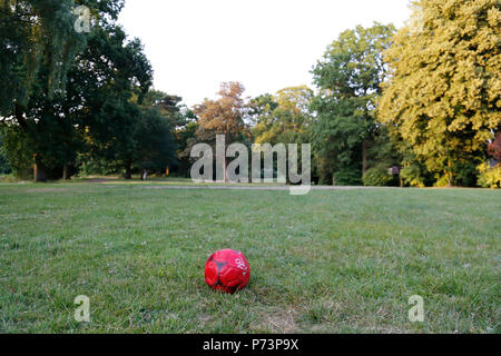 Football rouge dégonflé, abandonné dans le parc Banque D'Images