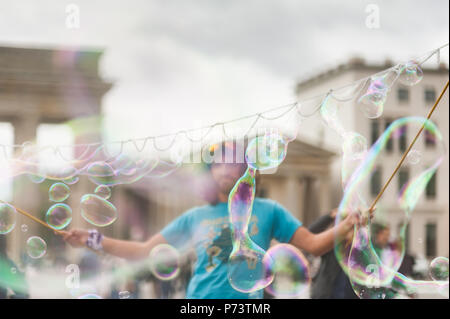 Bulles de savon coloré flottant dans l'avant-plan. Artiste de rue, musicien ambulant, divertissant la foule devant la porte de Brandebourg à Berlin. Banque D'Images