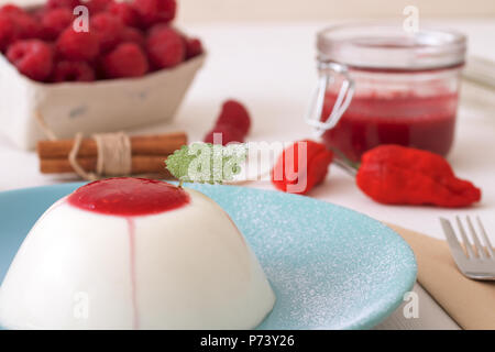 Panna Cotta (dessert italien sucré traditionnel, avec de la purée de framboises et touche de rouge piment Bhut jolokia chaud et de cannelle, décoré avec la feuille de fre Banque D'Images