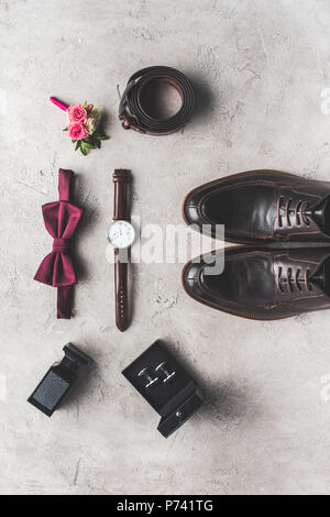 Vue de dessus du noeud papillon, boutonnière, une montre-bracelet et des chaussures pour mariage sur surface grise Banque D'Images