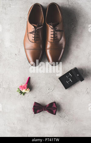 Vue de dessus de chaussures brunes, boutons de manchette, noeud papillon et boutonnière sur la surface gris Banque D'Images