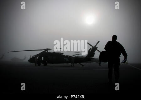 Un pilote instructeur promenades sur la piste pendant que les équipes de maintenance contrôle à l'UH-60M hélicoptère Black Hawk de l'armée, de l'Héliport à Lowe Fort Rucker, en Alabama dans un épais brouillard qui a recouvert la partie inférieure de l'état pendant plusieurs heures le matin du 9 mai, 2013. L'entretien du matériel existant est indispensable pour que de faibles coûts d'opération pour l'aéronef qui a été utilisé dans le monde entier pour les trois dernières décennies. Banque D'Images