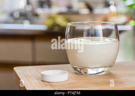 Verser la main le kéfir frais probiotik verre bouteilles en verre transparent, sur une table de cuisine. Banque D'Images