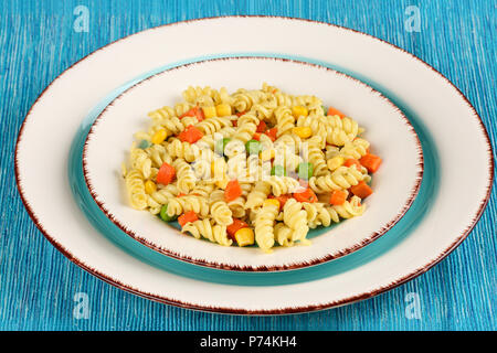 Maison délicieux cuisinés avec des fusillis au pesto de basilic, carottes, maïs et les petits pois dans une assiette sur une serviette bleu turquoise Banque D'Images