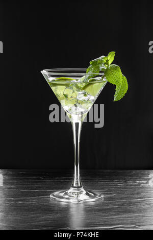 Cocktail d'été frais avec des tranches de citron vert, de la glace concassée et de feuilles de menthe dans un verre à martini sur fond noir rétroéclairé Banque D'Images