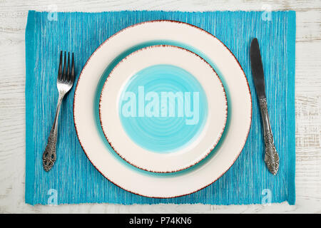 Vue de dessus d'une paire de salade vide et plats de dîner avec un bleu sarcelle et bien vintage fourchette et couteau sur une serviette turquoise et blanc en bois peint ta Banque D'Images