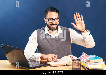 Homme barbu aux cheveux noirs l'apprentissage de l'anglais, le port de chandail gris veste et chemise blanche immaculée, mis en place la main avant de mur noir Banque D'Images