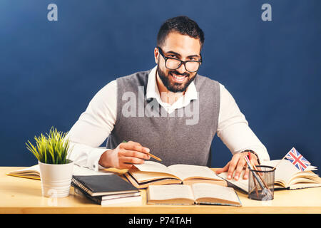 Homme barbu de l'Est travaillant dur apprentissage de l'anglais, le port de gilet chandail gris et une chemise blanche, d'un bureau avant de mur noir Banque D'Images