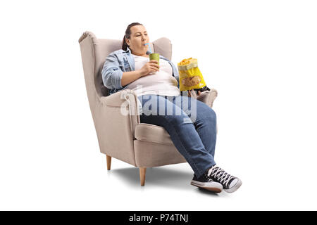 L'excès de femme avec un verre et un sac de chips assise sur un fauteuil isolé sur fond blanc Banque D'Images