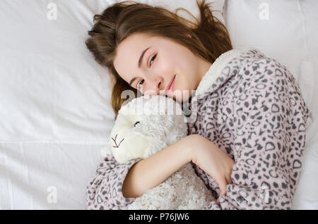 Jeune femme aux cheveux blonds dormant dans une étreinte avec un animal en peluche jouet. Moutons préférés dans les mains de teen girl in mignon pyjama chaud clo Banque D'Images