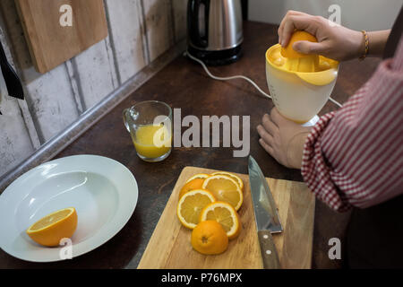 Petit jeune homme debout près de comptoir de la cuisine et l'aide pour faire du jus jus délicieux de l'orange. Banque D'Images